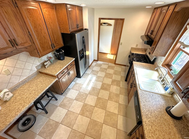 kitchen with brown cabinetry, appliances with stainless steel finishes, light countertops, baseboards, and a sink