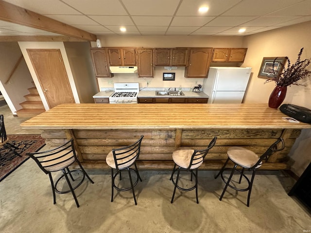 kitchen featuring a breakfast bar, white appliances, a drop ceiling, light countertops, and under cabinet range hood