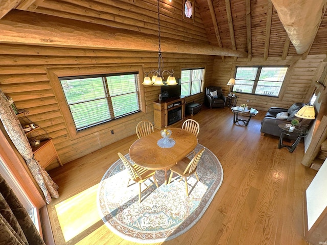 dining room with a chandelier, vaulted ceiling with beams, wood finished floors, rustic walls, and wood ceiling