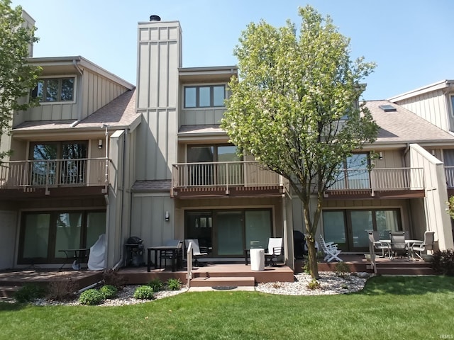 rear view of house featuring a lawn, a shingled roof, a chimney, and a balcony