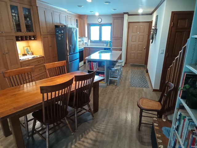 kitchen with a kitchen island with sink, light wood-type flooring, a sink, stainless steel fridge with ice dispenser, and light countertops