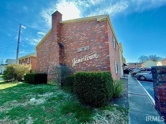 view of side of property with brick siding, uncovered parking, and a chimney
