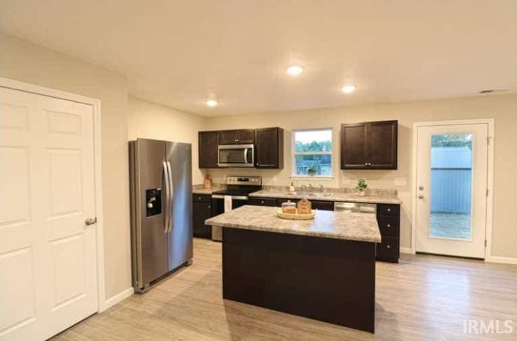 kitchen with a center island, light wood finished floors, appliances with stainless steel finishes, and baseboards