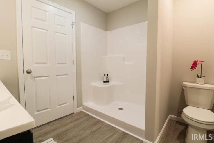 bathroom with vanity, a shower, wood finished floors, toilet, and baseboards