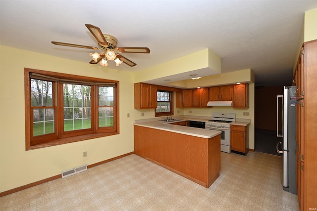800 E Oak View Est, Winamac, IN 46996 - kitchen with white gas range oven, a sink, a peninsula, under cabinet range hood, and visible vents