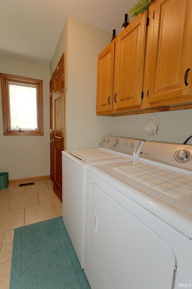 clothes washing area featuring washer and dryer, visible vents, and cabinet space