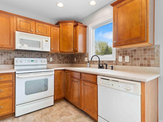 kitchen featuring brown cabinets, a sink, light countertops, recessed lighting, and white appliances