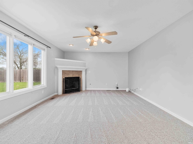 unfurnished living room with baseboards, a ceiling fan, a tile fireplace, and light colored carpet