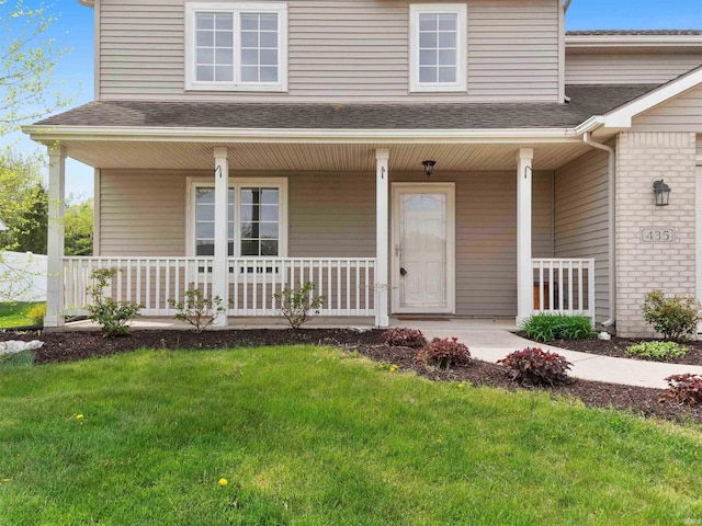entrance to property featuring a lawn, roof with shingles, and covered porch