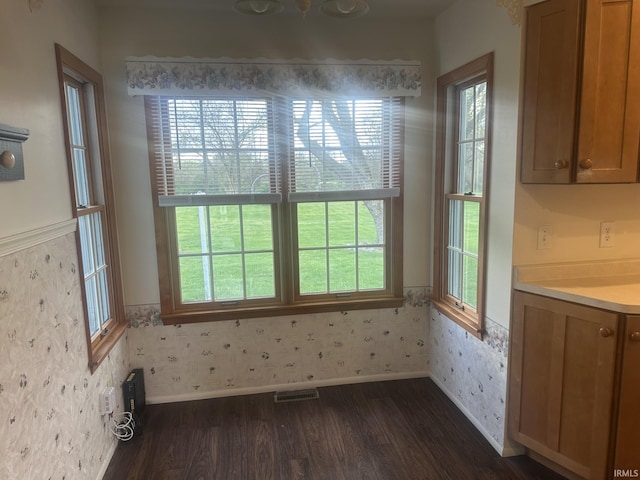 unfurnished dining area featuring visible vents, plenty of natural light, dark wood finished floors, and a wainscoted wall