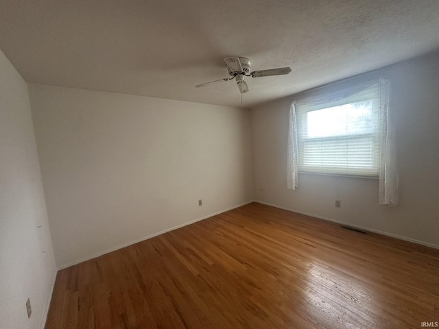 spare room with visible vents, a ceiling fan, baseboards, and wood finished floors