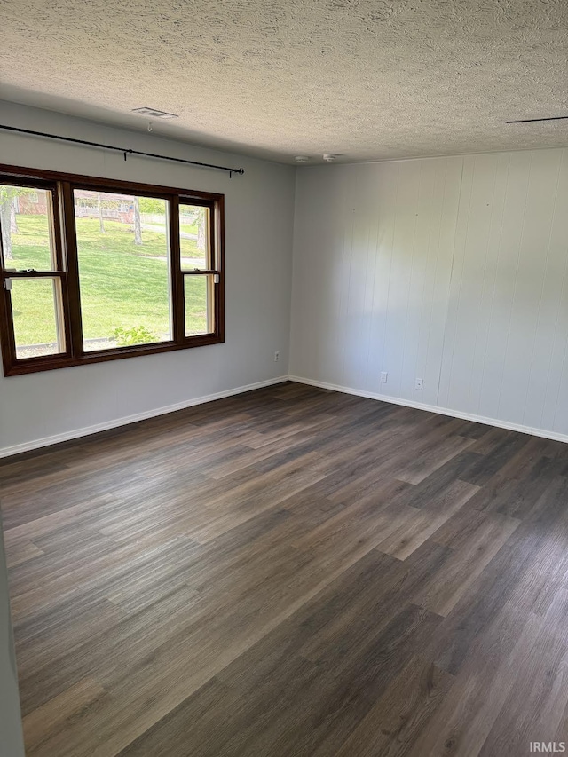 spare room featuring dark wood-style flooring, a textured ceiling, visible vents, and baseboards