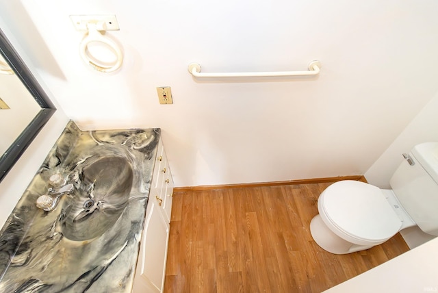 half bath with vanity, baseboards, wood finished floors, and toilet