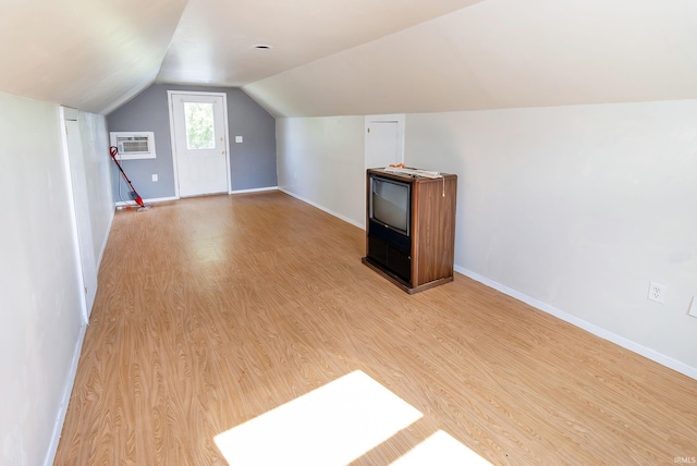 bonus room with baseboards, a wall unit AC, vaulted ceiling, and light wood finished floors