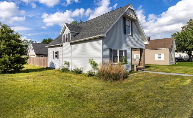 view of side of home with a lawn, fence, and roof with shingles