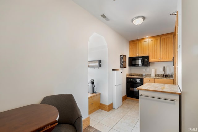 kitchen with a sink, baseboards, light tile patterned floors, visible vents, and black appliances