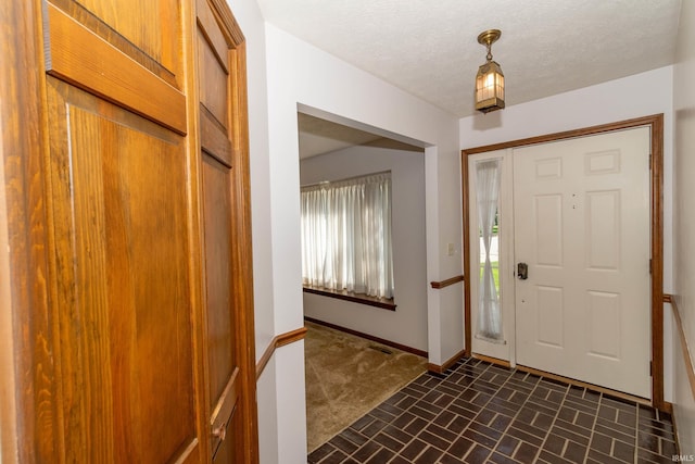 entrance foyer featuring baseboards, a textured ceiling, brick floor, and visible vents