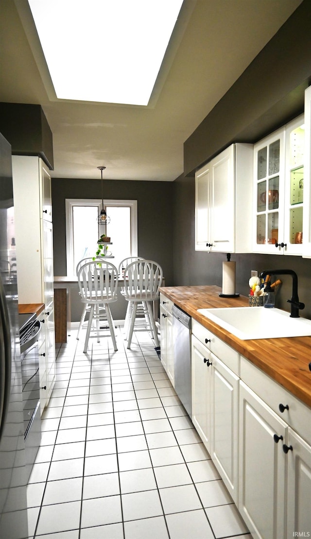 kitchen featuring butcher block countertops, a sink, white cabinetry, and dishwasher