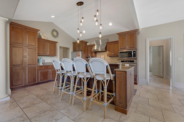kitchen featuring vaulted ceiling, wall chimney range hood, stainless steel appliances, and brown cabinets
