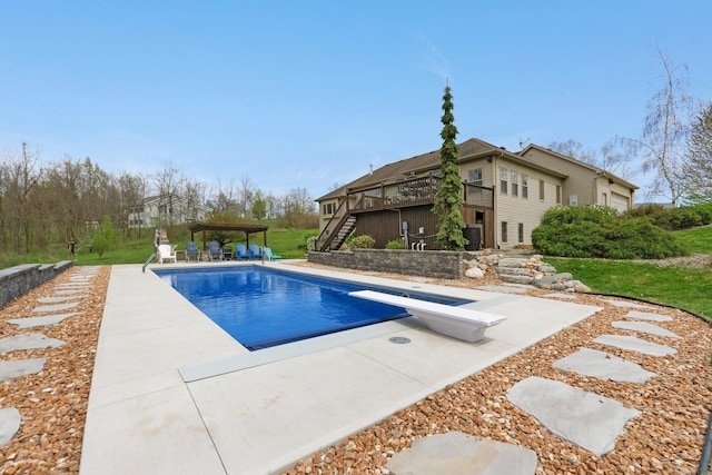 outdoor pool with stairs, a diving board, a patio area, and a deck