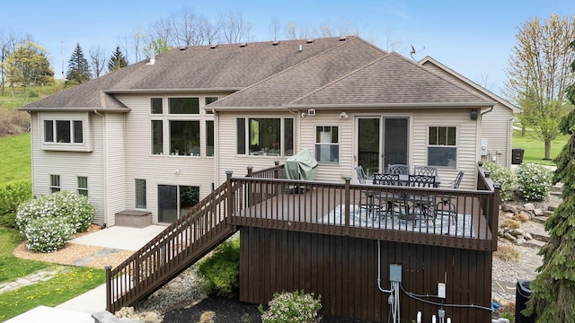 rear view of house with roof with shingles, a deck, a patio area, and stairway