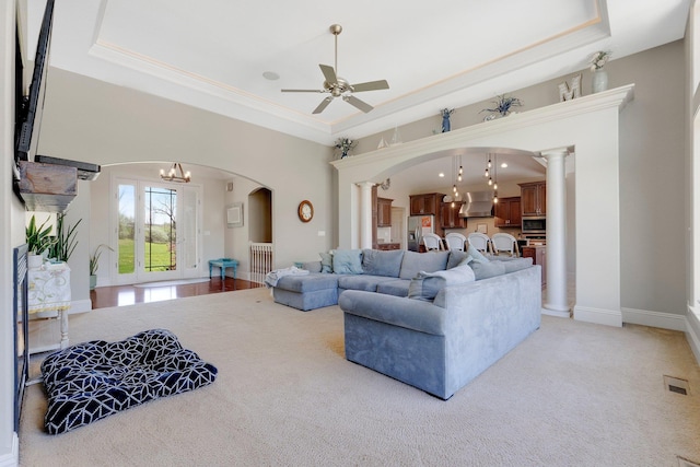 living room with visible vents, arched walkways, a raised ceiling, and ceiling fan with notable chandelier
