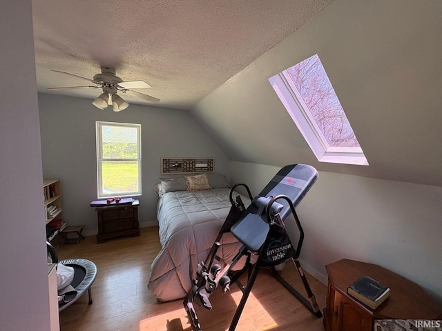 bedroom with vaulted ceiling with skylight, a textured ceiling, ceiling fan, and wood finished floors