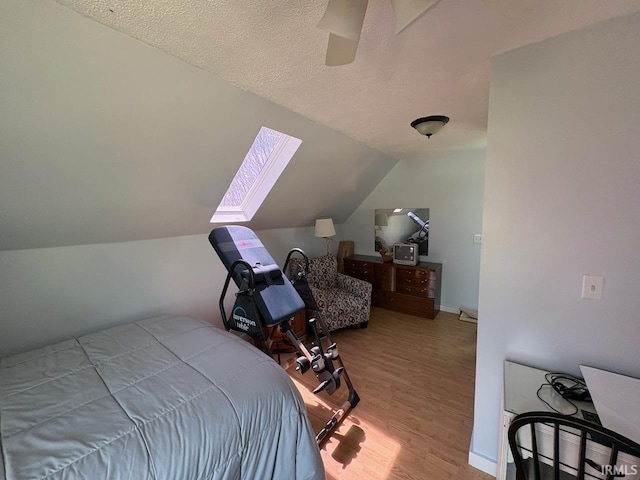 bedroom with a textured ceiling, lofted ceiling with skylight, wood finished floors, and ceiling fan