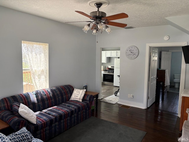 living room with a textured ceiling, a ceiling fan, baseboards, visible vents, and dark wood-style floors