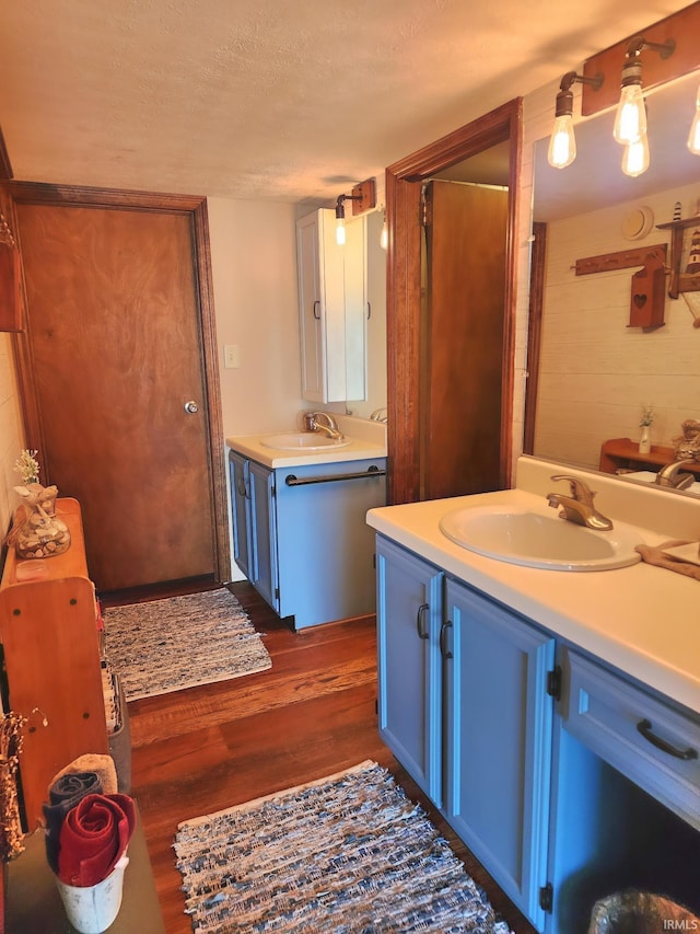 bathroom featuring a sink, a textured ceiling, wood finished floors, and two vanities