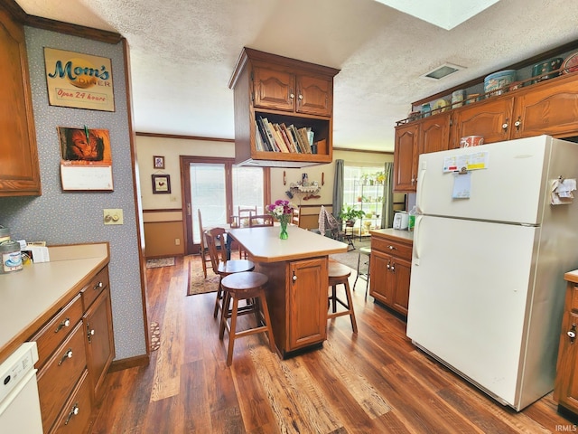 kitchen with white appliances, a kitchen bar, light countertops, a textured ceiling, and dark wood finished floors