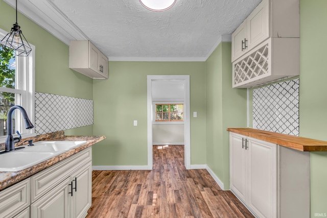 kitchen featuring ornamental molding, a textured ceiling, white cabinetry, a sink, and dark wood finished floors