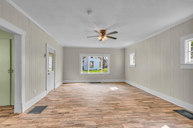 unfurnished room featuring a wealth of natural light, ornamental molding, wood finished floors, and visible vents