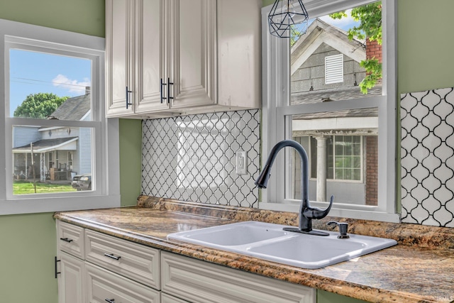 kitchen featuring backsplash, white cabinetry, a wealth of natural light, and a sink