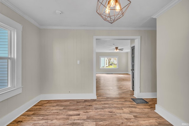 empty room featuring visible vents, wood finished floors, baseboards, a notable chandelier, and ornamental molding