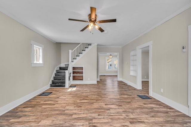 unfurnished living room with crown molding, ceiling fan, stairs, and wood finished floors