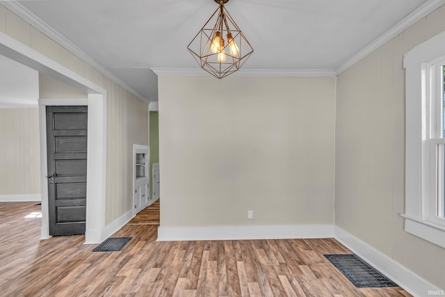 empty room featuring baseboards, visible vents, ornamental molding, and wood finished floors
