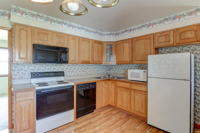 kitchen with glass insert cabinets, light wood-type flooring, light countertops, a sink, and black appliances