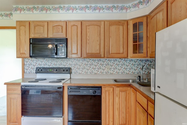 kitchen with light brown cabinetry, glass insert cabinets, light countertops, a sink, and black appliances