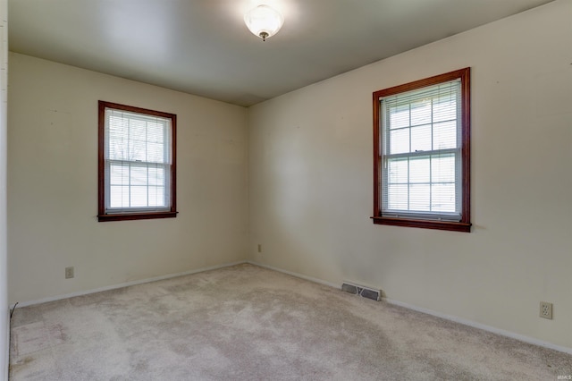 spare room with plenty of natural light, baseboards, visible vents, and light colored carpet