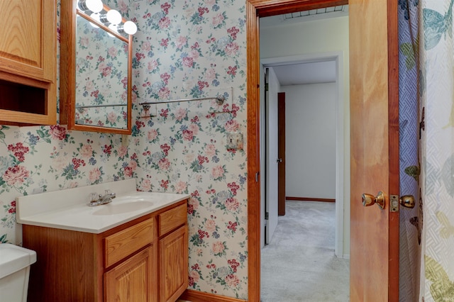 half bathroom featuring toilet, wallpapered walls, baseboards, and vanity