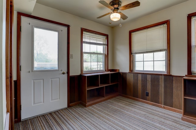 doorway featuring carpet flooring, ceiling fan, a wealth of natural light, and a wainscoted wall