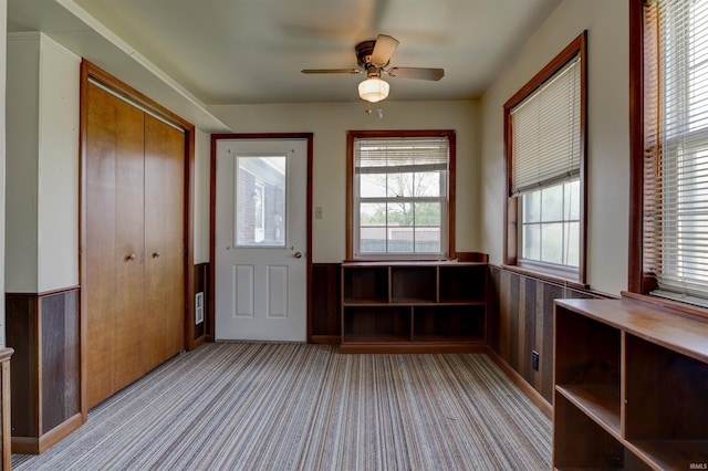 interior space with a wainscoted wall, ceiling fan, and light colored carpet
