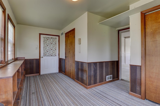 interior space with carpet floors, wooden walls, visible vents, and a wainscoted wall