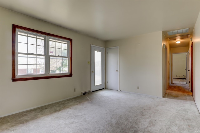 unfurnished room with visible vents, attic access, baseboards, and light colored carpet