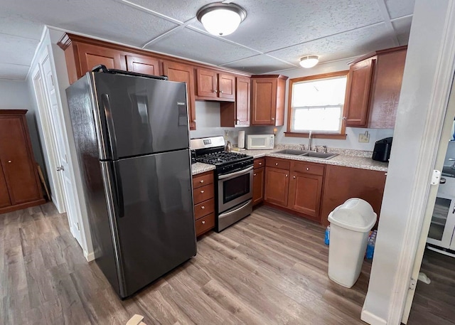 kitchen with stainless steel gas range oven, a sink, freestanding refrigerator, white microwave, and light wood-style flooring