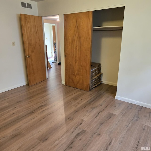 unfurnished bedroom featuring baseboards, visible vents, wood finished floors, and a closet