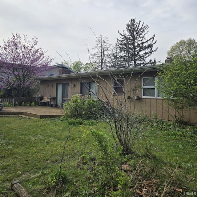 back of house with a lawn, a deck, and a chimney