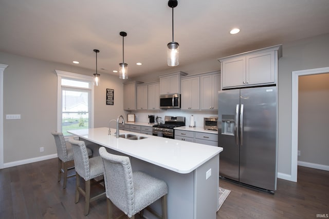 kitchen featuring gray cabinets, a center island with sink, a sink, baseboards, and stainless steel appliances