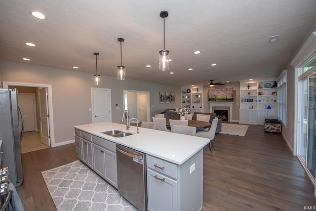 kitchen featuring ceiling fan, a kitchen island with sink, a fireplace, a sink, and stainless steel appliances